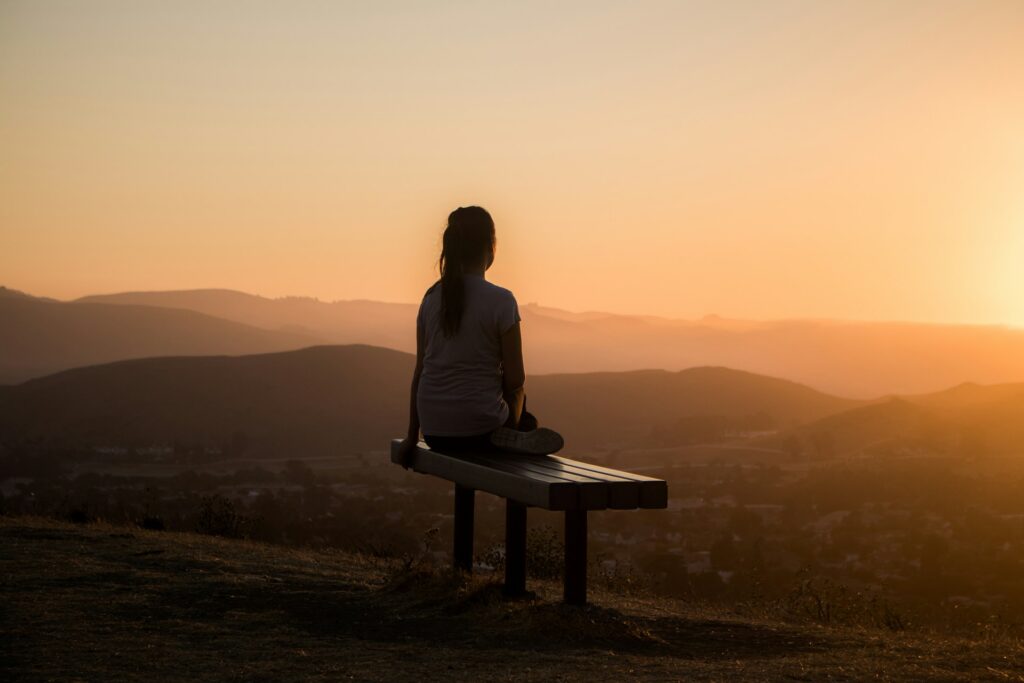viaggiare lentamente significa anche introspezione. Questa donna è seduta su una panchina ed osserva un tramonto 